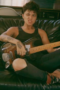 a man sitting on top of a black couch holding a guitar and looking at the camera