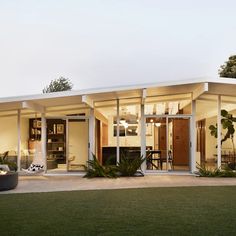 a modern house with glass walls and plants in the front yard at dusk, lit up by lights