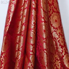 red and gold brocaded fabric with large flowers on the bottom, in front of a white background