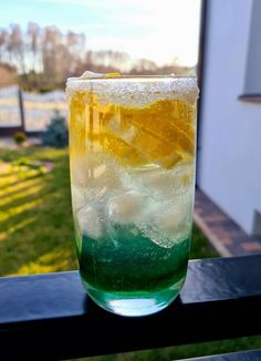 a tall glass filled with liquid sitting on top of a wooden table next to a window