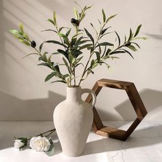 a white vase sitting next to a wooden hexagonal object with flowers in it