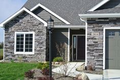 a gray house with two garage doors and green grass in the front yard, on a sunny day