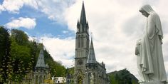 there is a statue in front of the building with many spires and flowers around it