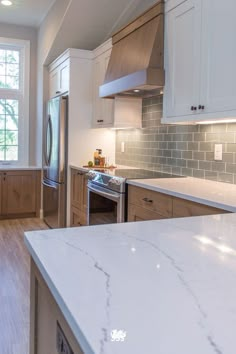 a kitchen with white cabinets and marble counter tops