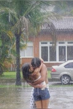 a man and woman hugging in the rain outside their house with cars parked behind them