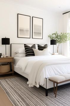 a white bedroom with black and white decor on the bed, two framed pictures above the bed