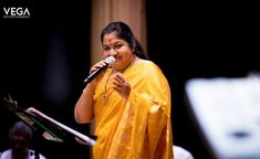 a woman in a yellow sari singing into a microphone