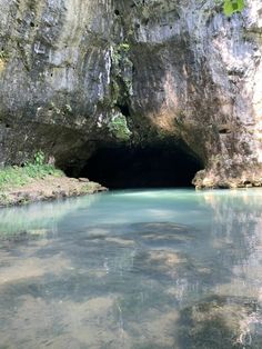 the water is crystal blue and clear in this cave area, with green vegetation growing on both sides