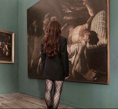 a woman standing in front of a painting looking at the art on display behind her