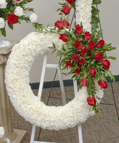 white and red flowers are arranged in a circular arrangement on a pedestal next to a chair