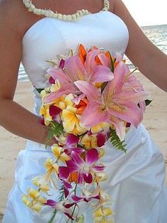 a bride holding a bouquet of flowers on the beach