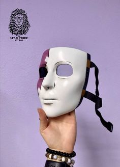 a person holding up a white mask in front of a purple wall