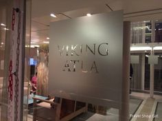 a glass sign that says waking at ata in front of a building with people walking by