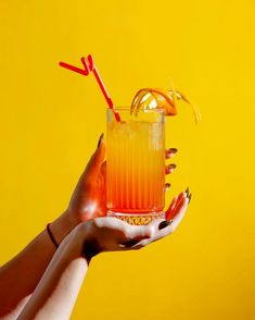 a woman holding a drink with orange and red sticks sticking out of it's top