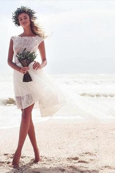 a woman standing on top of a sandy beach next to the ocean holding a bouquet of flowers