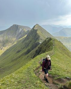 a man hiking up the side of a lush green mountain covered in lots of grass