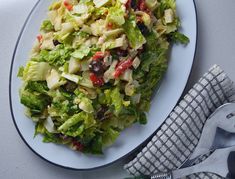 a white plate topped with salad next to a fork and knife on top of a table