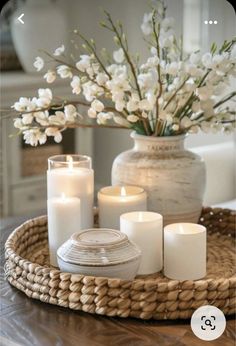 a wicker tray with white candles and flowers in it on top of a table