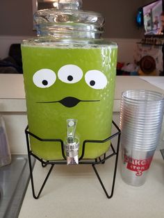 a green beverage dispenser sitting on top of a counter next to plastic cups