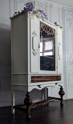 a white cabinet with purple flowers on the top and bottom, sitting in front of a wall