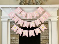 a pink happy birthday banner hanging over a fireplace