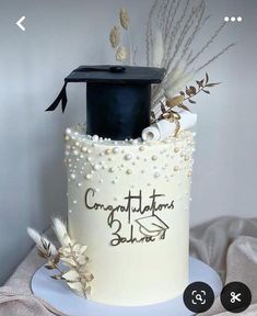 a graduation cake decorated with pearls, feathers and a mortar cap on top of it