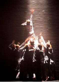 a group of people standing on top of each other in front of a brick wall