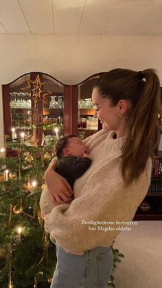 a woman holding a baby in front of a christmas tree