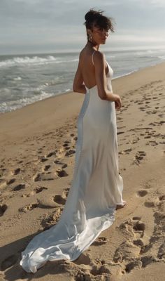 a woman standing on top of a sandy beach next to the ocean wearing a white dress