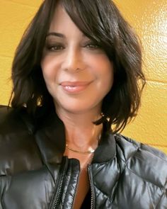 a woman wearing a black leather jacket and smiling at the camera with yellow wall behind her