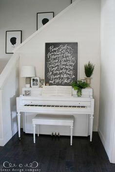 a white piano sitting in the corner of a room next to a stair case with writing on it