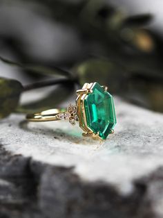 an emerald colored stone ring sitting on top of a piece of rock next to a plant