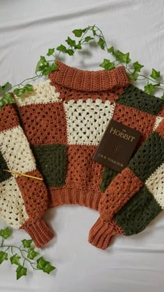 a knitted sweater with a book on it sitting on a bed next to ivy