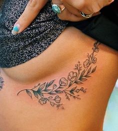 a woman's lower back tattoo with flowers and leaves on her stomach, showing the side