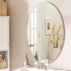 a bathroom sink with a large round mirror over it's top shelf next to a white cabinet