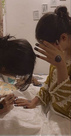 two women sitting on a bed with their hands in the air while one woman holds her phone up to her ear