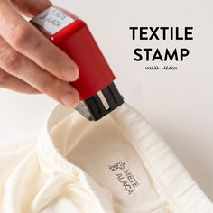 a person using a red stapler to attach a white shirt with the words textile stamp on it