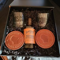 an orange bottle and two shot glasses are in a gift box with some other items