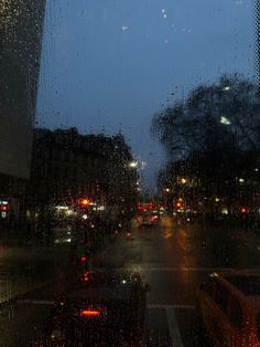 the rain is falling down on the city street at night as cars drive by in the distance