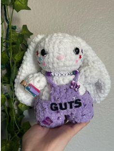 a hand holding a small stuffed animal with the word guts on it's chest