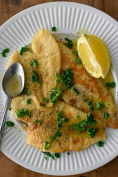 a white plate topped with fish covered in sauce and garnished with parsley