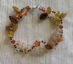 a beaded bracelet with leaves and beads is shown on a white surface, it has the word fall written in small letters