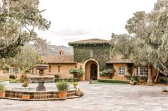 an old spanish style house with a fountain in the front yard, surrounded by trees