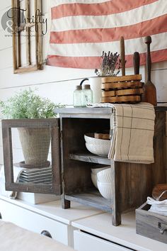 an old wooden cabinet with dishes and utensils on it in front of the american flag