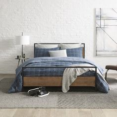 a bedroom with white brick walls and wood flooring is furnished with a bed that has blue plaid sheets, pillows, and throw pillows