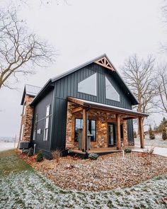 a small black house with stone and wood accents in the front yard on a snowy day