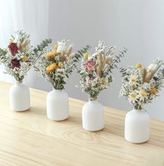 four white vases with flowers in them sitting on a table