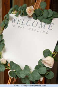 a welcome sign with flowers and greenery around it