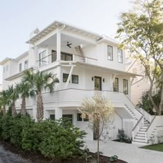 a white two story house with palm trees in the front yard and stairs leading up to it