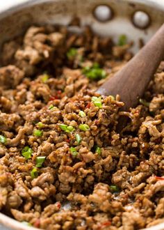 a wooden spoon mixing meat in a pan with onions and green peppers on the side